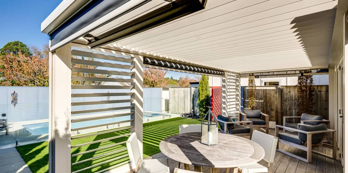 An outdoor room showing louvre roof, panels and outdoor setting with pool views